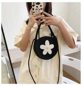 Détail du sac rond tissé noir orné d'une fleur blanche et d'une perle centrale