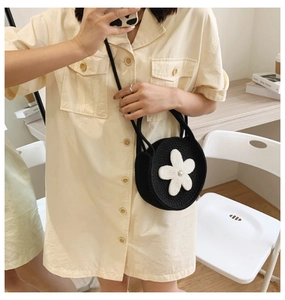 Détail d'un petit sac bandoulière rond en tricot noir avec une fleur blanche brodée
