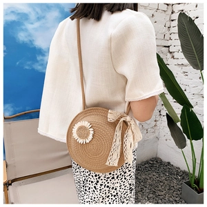 Detail of round straw crossbody bag with daisy applique and beige lace bow detail
