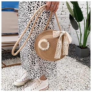 Close-up of circular straw bag with white lace bow and daisy floral decoration
