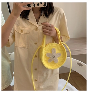 Gros plan du sac à main rond en tricot jaune orné d'une fleur blanche avec perle au centre