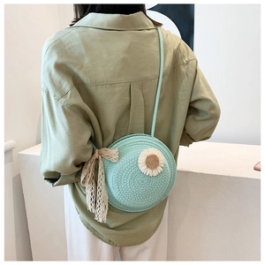 Detail of mint green woven round straw bag with white daisy and lace bow accent