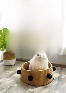 Detail of hand-woven cotton cat nest with pom-poms in a warm home setting