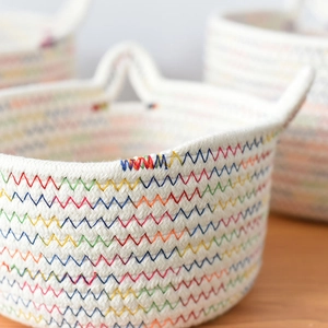 Detail of colorful rainbow stitching on white woven cotton rope basket with cat ears