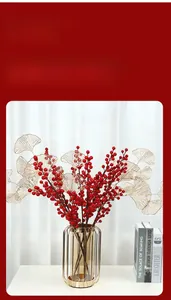 Close-up of red holly berries and golden ginkgo leaves in an amber glass vase