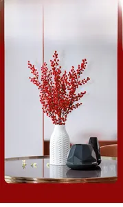 Close-up of red winterberries in white ceramic vase with geometric decor accents
