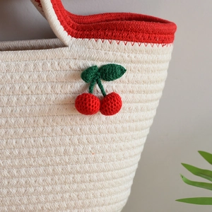 Detail view of woven straw tote bag with crochet cherry charms and red handle trim
