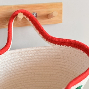 Close-up of woven cotton rope handbag with red handle detail on a wooden hook