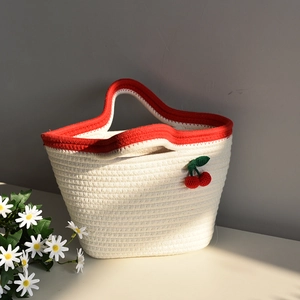 Detail of hand-woven cotton rope bag featuring crochet red cherry charm and contrast handles
