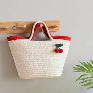 White cotton woven cherry tote bag with red trim hanging on a wooden wall hook