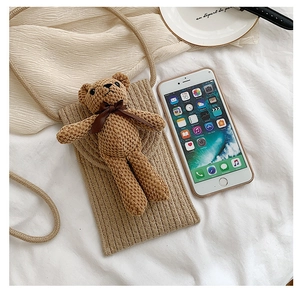 Close-up of khaki woven straw phone bag featuring a cute teddy bear charm on white cloth