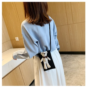 Detail of black straw woven phone bag featuring a 3D plush bear on a model's shoulder