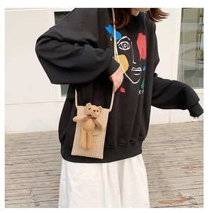 Close-up of beige straw woven crossbody phone bag featuring a cute plush bear decoration
