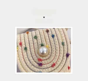 Detail of woven straw mini bag featuring colorful pom-poms and a large pearl button
