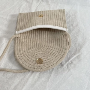 Close-up of woven crossbody bag with white leather trim and golden magnetic snap closure