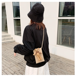 Detail of a beige straw shoulder bag with a cute plush bear and dark brown bow detail