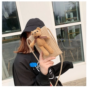 Close-up of beige woven phone bag with a cute brown teddy bear and bow detail