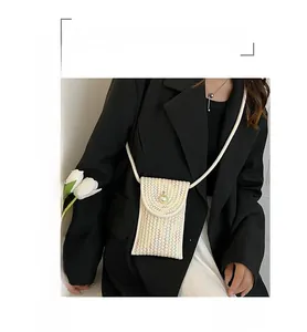 Detailed view of woven straw mini bag featuring a large pearl clasp and long shoulder strap