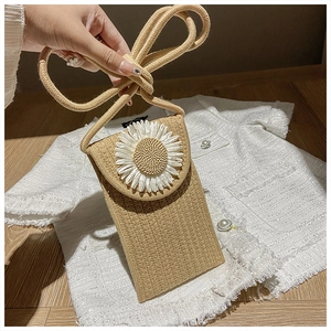 Detail of woven straw crossbody bag featuring a white daisy flower on a tweed background