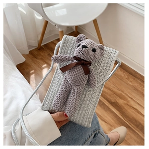 Close-up of handmade gray knitted straw bag with 3D cute bear and ribbon for mobile phone