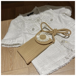 Close-up of khaki woven crossbody bag with white daisy flower detail on tweed background