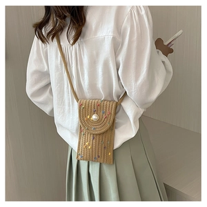 Detail of a woven straw mini phone bag with colorful tassels and a large faux pearl button