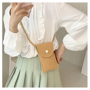 Detail of woven straw mini bag featuring a large pearl button and natural texture
