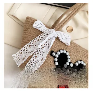 Détail avec nœud en dentelle, lunettes en perles et lèvres brodées sur sac tissé beige