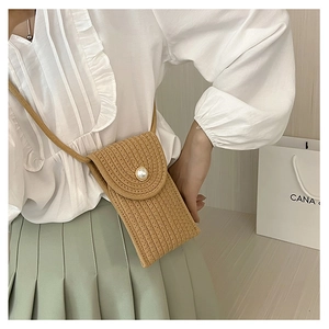 Detail of a mini straw woven phone bag with a pearl buckle and slender shoulder strap