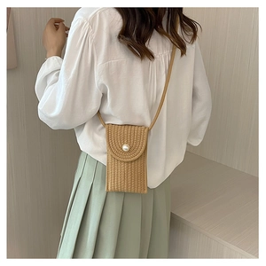 Detail of khaki straw mini crossbody bag featuring a woven texture and pearl closure buckle
