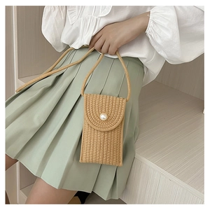 Detail of hand-woven mini straw crossbody bag with pearl buckle on white ruffled shirt
