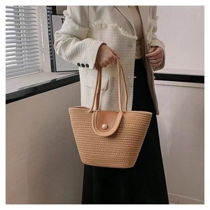 Detail of woven straw tote bag featuring a leather flap and elegant pearl closure