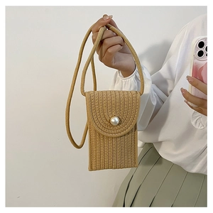 Detail of khaki straw mini bag featuring a large decorative pearl and thin shoulder strap