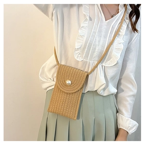 Detail of straw woven mini bag with pearl buckle on model with ruffled white shirt