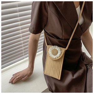 Detail of woven straw crossbody phone bag featuring a white daisy flower decoration