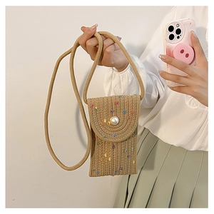 Detail of straw woven mini bag with faux pearl closure and colorful fiber accents