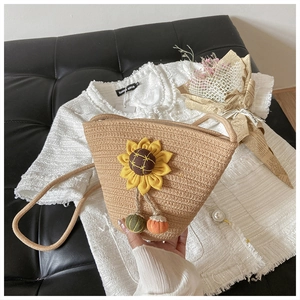 Detailed close-up of handmade straw bucket bag with sunflower applique and colorful pompom charms
