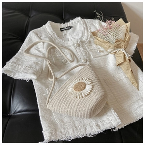 Flat lay of a woven daisy bag with a white tweed top and pearl buttons on black leather