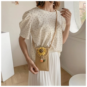 Detail of hand-woven straw phone bag with sunflower ornament and pom-pom tassel
