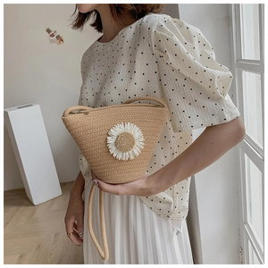 Close-up of a straw bucket bag featuring a large white daisy flower and slim shoulder strap