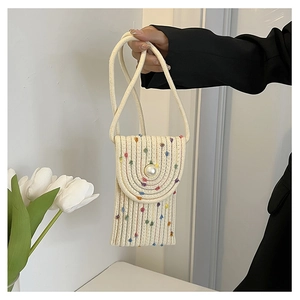 Detail of hand-woven mini straw bag with colorful pom-poms and large pearl button