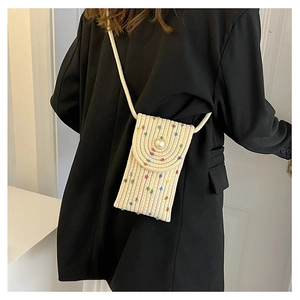 Detail of hand-woven mini straw phone bag with pearl button closure on black suit