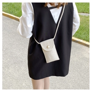 Detail of straw woven phone bag with large pearl closure on creamy white crossbody strap