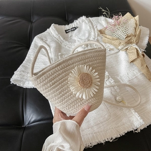 Detail view of woven straw bucket bag featuring a large white daisy flower and thin strap