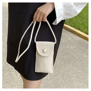 Detailed view of woven straw mini bag featuring a large pearl clasp and rope strap