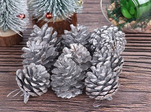 Cluster of nine silver pine cone ornaments with silver hanging strings on dark wood surface