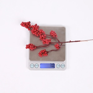 Macro detail of artificial red berry branch on electronic scale weighing 7.0g