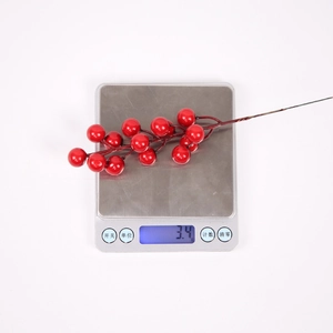 Close-up of artificial red berry branch on a scale showing 3.4g weight for decor