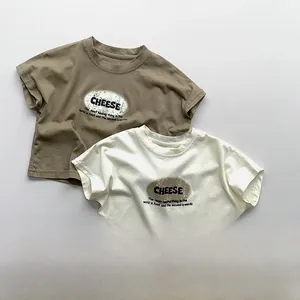 Flat lay of two kids' cotton t-shirts in khaki brown and cream white with cheese print