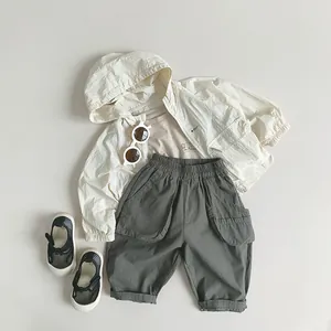 Flat lay of kids lightweight beige hooded jacket with olive green shorts and black shoes